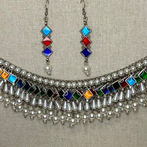 Peut inclure: Un collier en argent avec un motif de carreaux de verre multicolores et des accents de perles blanches. Le collier est assorti d'une paire de boucles d'oreilles avec le m&ecirc;me motif.