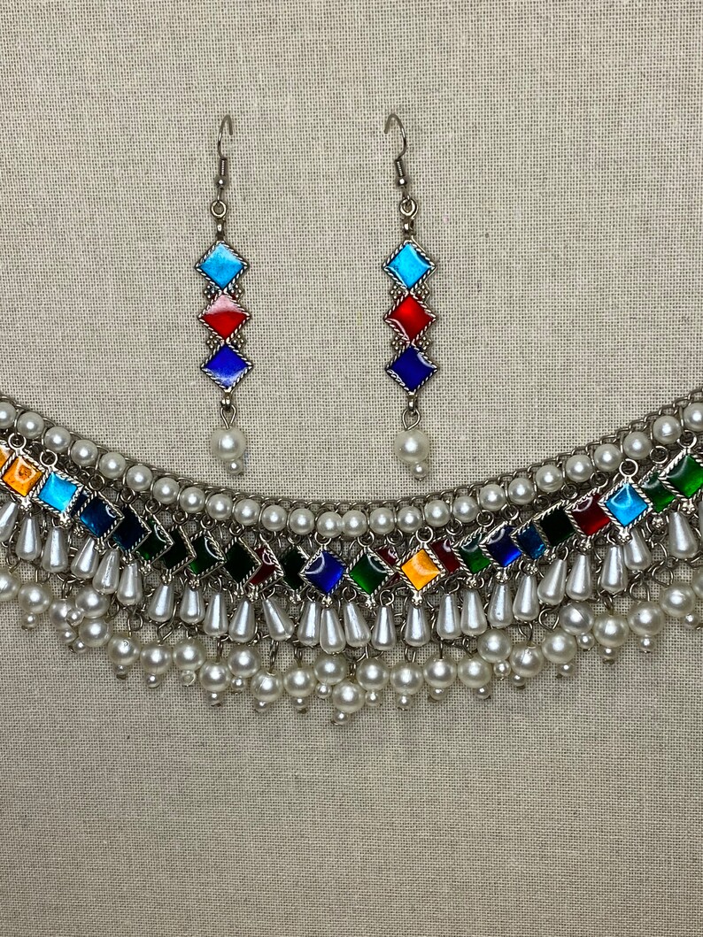 Peut inclure: Un collier en argent avec un motif de carreaux de verre multicolores et des accents de perles blanches. Le collier est assorti d'une paire de boucles d'oreilles avec le m&ecirc;me motif.