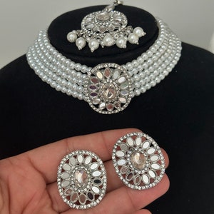 The silver color choker has white pearls and mirror work on earrings, tikka, and centrepiece.