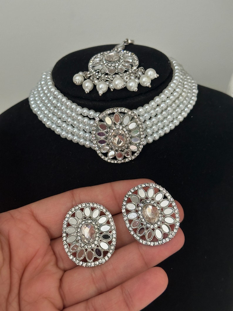 The silver color choker has white pearls and mirror work on earrings, tikka, and centrepiece.