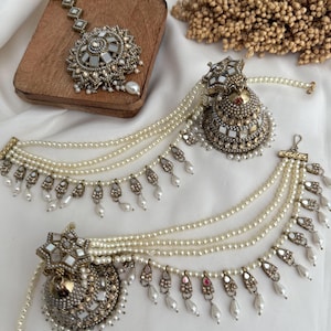 Könnte beinhalten: Ein aufwendiges Brautschmuck-Set im antiken Stil. Das Set umfasst einen Kopfschmuck und Ohrringe mit aufwendigen Metallarbeiten, Spiegelakzenten und herabhängenden Perlenschnüren. Die Stücke werden auf weißem Stoff präsentiert.