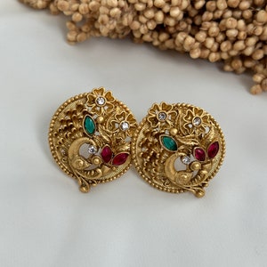 Puede incluir: Un par de pendientes de tono dorado con un dise&ntilde;o de pavo real. Los pendientes est&aacute;n adornados con piedras preciosas verdes y rojas y diamantes de imitaci&oacute;n blancos.