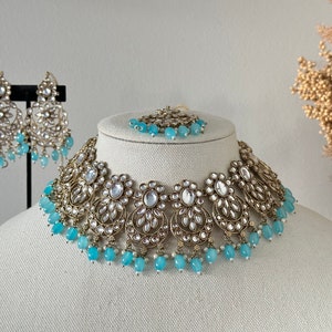 May include: A gold and silver necklace with blue beads and a matching pair of earrings. The necklace is made of intricate metalwork and features a floral design.