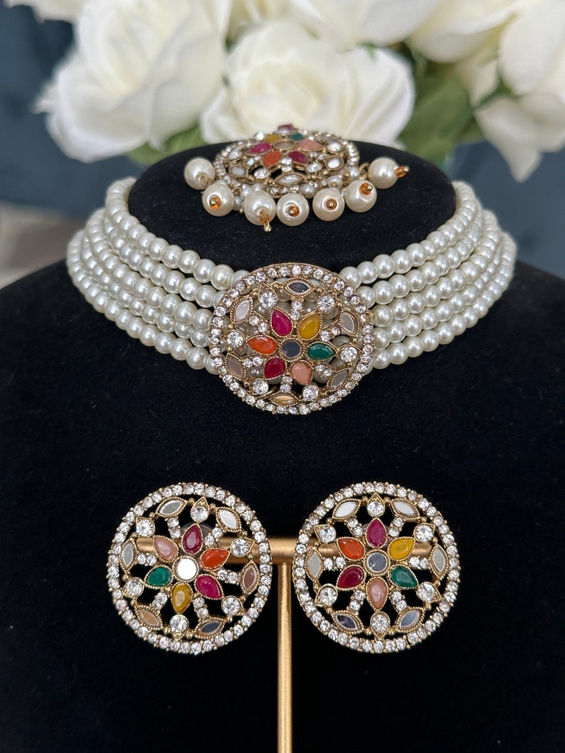 This choker has off- white pearls, stone and Kundan work on studs, central piece and tikka.