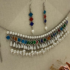 Peut inclure: Un collier en argent avec une rang&eacute;e de carreaux carr&eacute;s color&eacute;s et une frange de perles blanches. Boucles d'oreilles assorties avec trois carreaux carr&eacute;s color&eacute;s et une seule perle pendante.