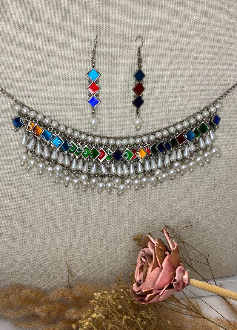 Peut inclure: Un collier en argent avec un motif en &eacute;mail multicolore et des accents de perles blanches. Le collier a un design en couches avec plusieurs rang&eacute;es de perles. Le collier est assorti &agrave; des boucles d'oreilles avec un design en &eacute;mail multicolore similaire.