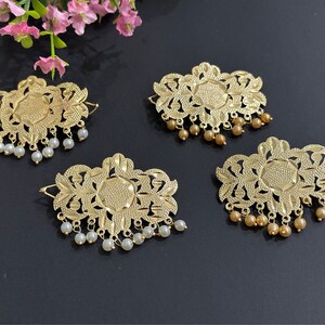 May include: Four gold-colored hair clips with intricate floral designs. Each clip has a row of small white or gold beads hanging from the bottom.