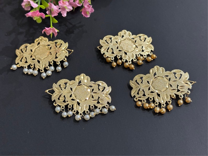 May include: Four gold-colored hair clips with intricate floral designs. Each clip has a row of small white or gold beads hanging from the bottom.