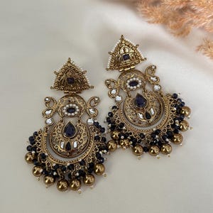 May include: A pair of gold-tone earrings with intricate designs, featuring blue and white stones, and black beads dangling from the bottom.