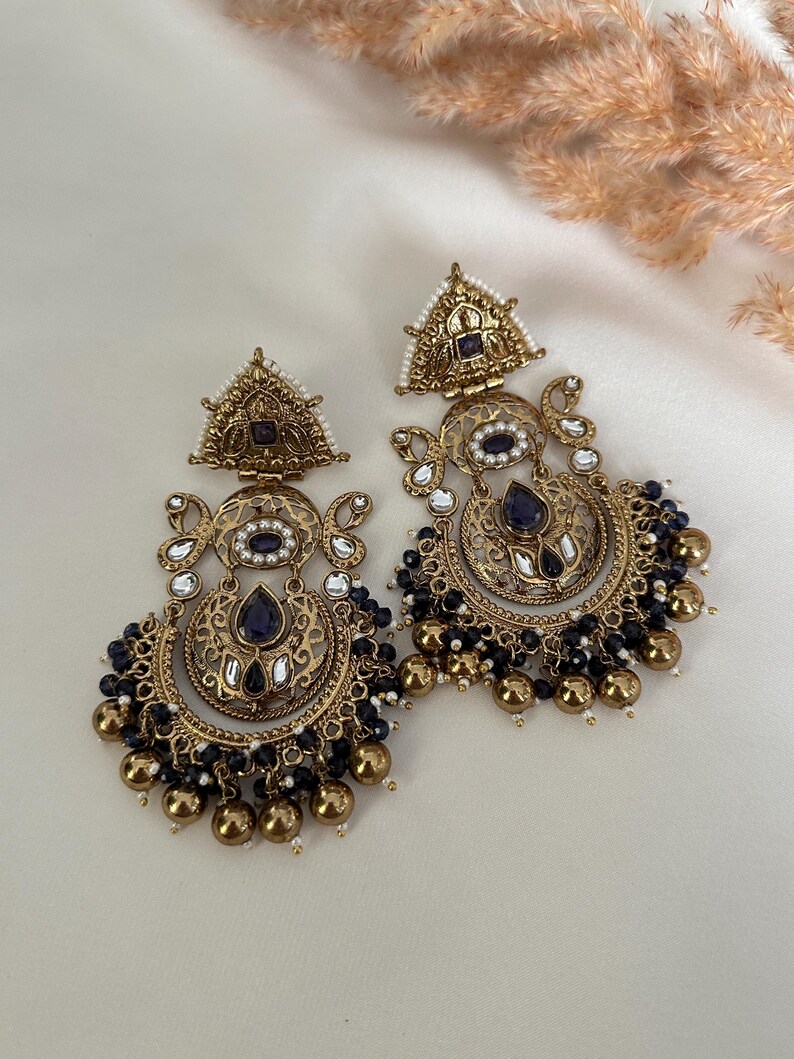 May include: A pair of gold-tone earrings with intricate designs, featuring blue and white stones, and black beads dangling from the bottom.