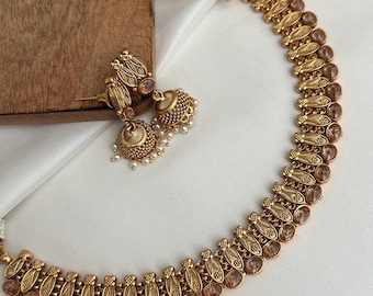 May include: A gold necklace with brown stones and matching earrings. The necklace is made of intricate metalwork and features a repeating pattern of leaves and stones.