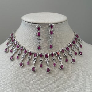 May include: A silver necklace and earrings set with dangling ruby and clear crystal accents.