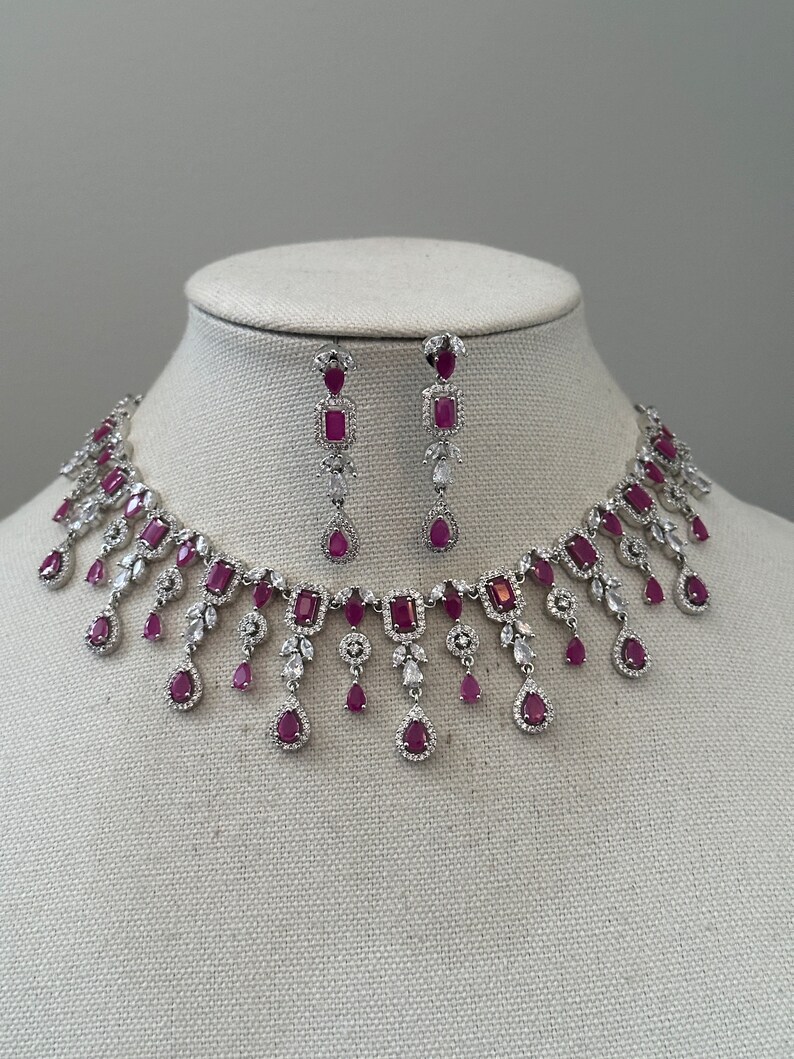 May include: A silver necklace and earrings set with dangling ruby and clear crystal accents.