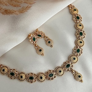 Puede incluir: Un collar y pendientes de oro con piedras verdes y transparentes. El collar tiene un colgante con una piedra verde y los pendientes tienen una sola piedra verde.