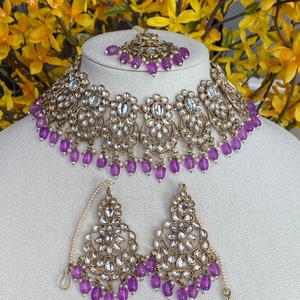 May include: A gold and silver necklace set with purple beads and clear stones. The necklace has a choker style and the earrings are dangle style.