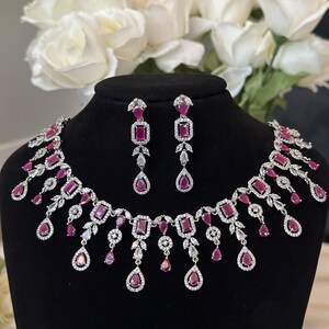 May include: A silver necklace and earrings set with pink gemstones and clear cubic zirconia. The necklace features a cascading design with teardrop-shaped pendants.