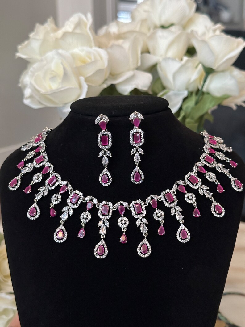 May include: A silver necklace and earrings set with pink gemstones and clear cubic zirconia. The necklace features a cascading design with teardrop-shaped pendants.