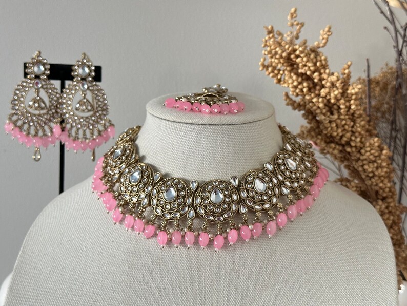 May include: A gold and silver necklace with pink beads and a matching pair of earrings. The necklace has a large, ornate design with multiple round pendants.