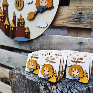 May include: A stack of wooden welcome favors featuring a cartoon character with red hair and a yellow scarf. The favors are decorated with a yellow castle and the text "Hos Geldin Yagmur".