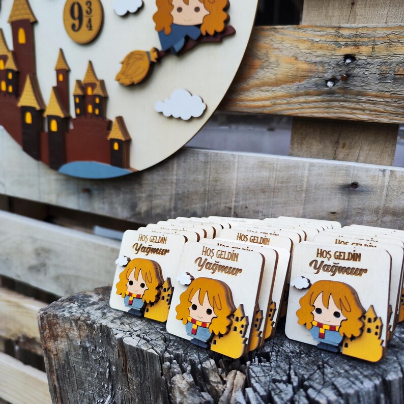 May include: A stack of wooden welcome favors featuring a cartoon character with red hair and a yellow scarf. The favors are decorated with a yellow castle and the text "Hos Geldin Yagmur".