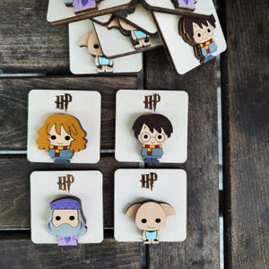 May include: Four wooden Harry Potter character pins with the text "HP" on each pin. The characters are Harry Potter, Hermione Granger, Ron Weasley, and Dobby the house elf.