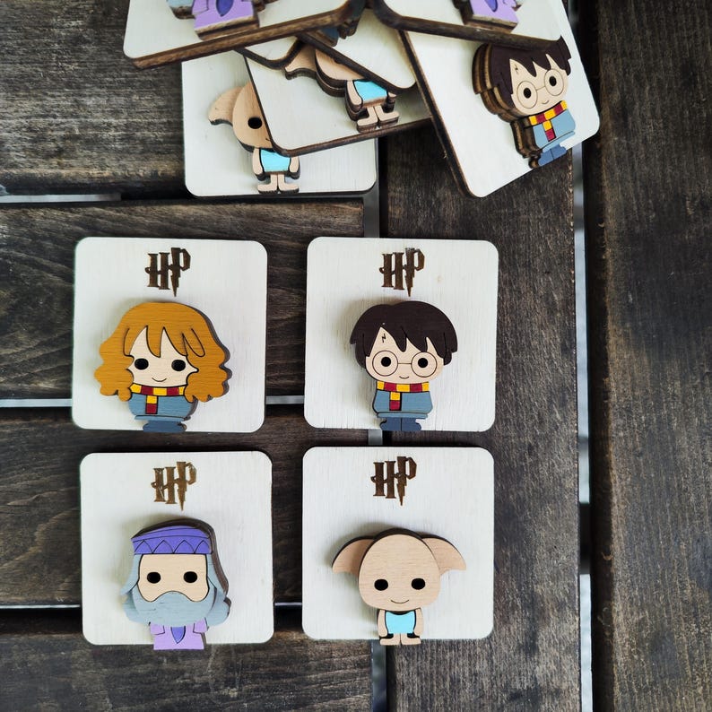 May include: Four wooden Harry Potter character pins with the text "HP" on each pin. The characters are Harry Potter, Hermione Granger, Ron Weasley, and Dobby the house elf.