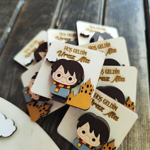 May include: A stack of wooden welcome signs with a cartoon character of Harry Potter. The signs are decorated with a castle and the text "HOŞ GELDİN Uraz Ata" in Turkish.