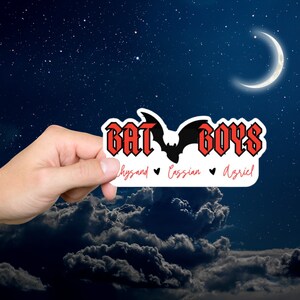 Pode incluir: Um adesivo vermelho e preto com o texto "Bat Boys" e uma silhueta de morcego. O texto "Rhysand, Cassian, Azriel" está escrito abaixo do morcego.