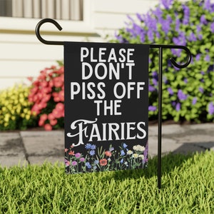 May include: A black garden flag with white text that reads "Please Don't Piss Off The Fairies". The flag has a border of colorful flowers.