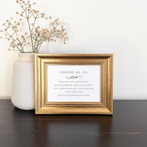 May include: A rectangular gold-toned picture frame containing a white print with black text that reads Isaiah 41:10, Fear not, for I am with you; be not dismayed, for I am your God; I will strengthen you, I will help you, I will uphold you.