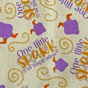 May include: A beige fabric with a repeating pattern of purple witches' hats and the text "One little spark of inspiration". The text is in a yellow, orange, and brown swirl font.