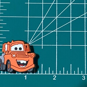 May include: Orange and gray cartoon tow truck with a smiling face. The tow truck is a character from the Disney Pixar movie Cars.