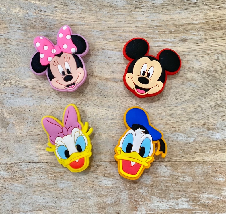 Może przedstawiać: Cztery kolorowe urocze breloczki z postaciami z kresk&oacute;wek, w tym Myszka Miki, Minnie Mouse, Donald Duck i Daisy Duck. Breloczki są wykonane z gumy i mają błyszczące wykończenie.