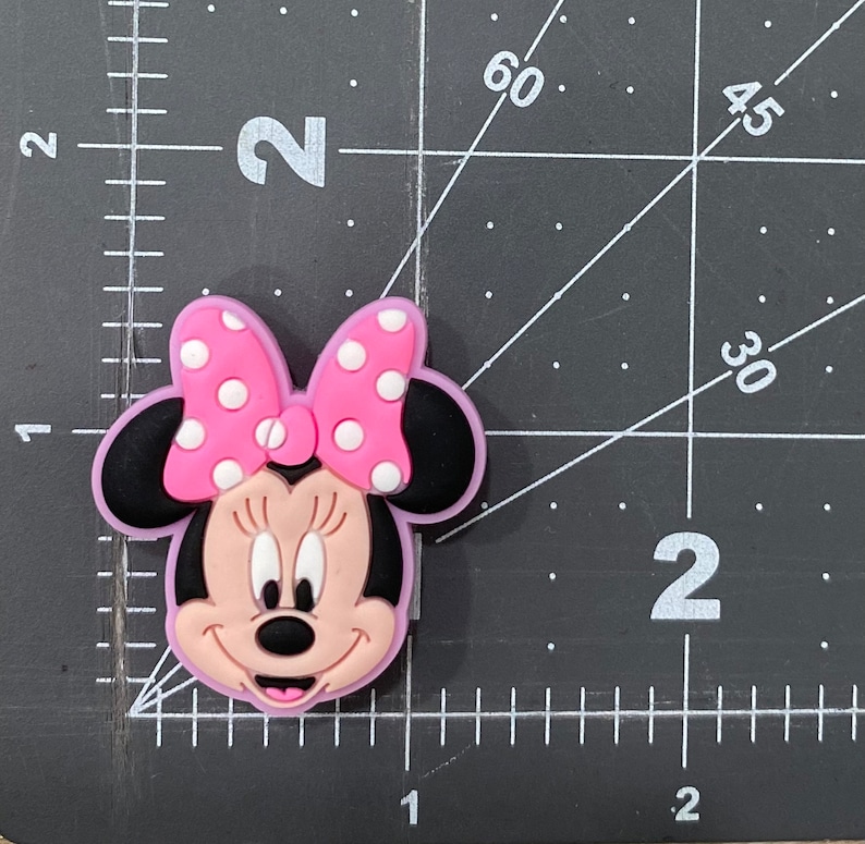 Może przedstawiać: Postać Minnie Mouse w kolorze r&oacute;żowym i czarnym z r&oacute;żową kokardką w białe kropki.