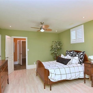 May include: A bedroom with a green wall, a white ceiling fan, a wooden bed with a white and black checkered comforter, a wooden bedside table, and a floor lamp with a white lampshade.