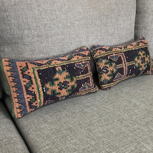 May include: Two rectangular throw pillows featuring a woven, textured surface with a dark navy blue, muted orange, and forest green geometric pattern. The pillows have a dense, knotted pile construction and are finished with simple, clean edges.