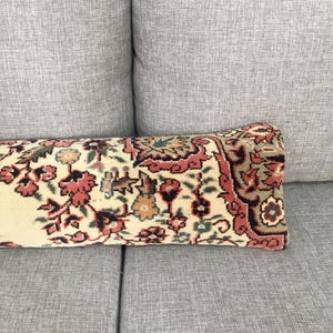 May include: A rectangular lumbar pillow featuring a woven textile cover with a dense floral and geometric pattern in shades of cream, muted red, dark green, and black. The design displays intricate botanical motifs and a decorative border.