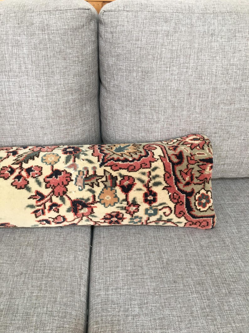 May include: A rectangular lumbar pillow featuring a woven textile cover with a dense floral and geometric pattern in shades of cream, muted red, dark green, and black. The design displays intricate botanical motifs and a decorative border.