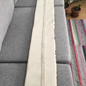 May include: A long, rectangular lumbar pillow cover featuring a solid off-white canvas fabric on the front side. The cover has a centered vertical seam running the entire length of the piece, with a hidden zipper closure integrated into the seam.