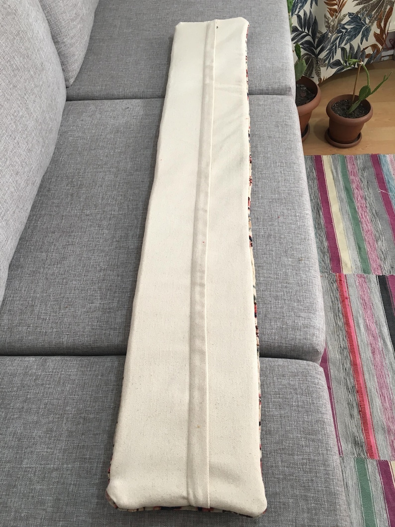 May include: A long, rectangular lumbar pillow cover featuring a solid off-white canvas fabric on the front side. The cover has a centered vertical seam running the entire length of the piece, with a hidden zipper closure integrated into the seam.