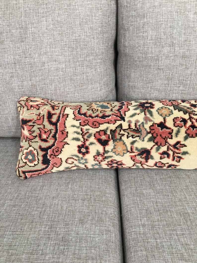 May include: A rectangular lumbar pillow featuring a woven textile cover with a dense floral pattern in shades of muted coral, dark navy blue, and sage green on a cream-colored background, showcasing intricate botanical motifs and ornate borders.