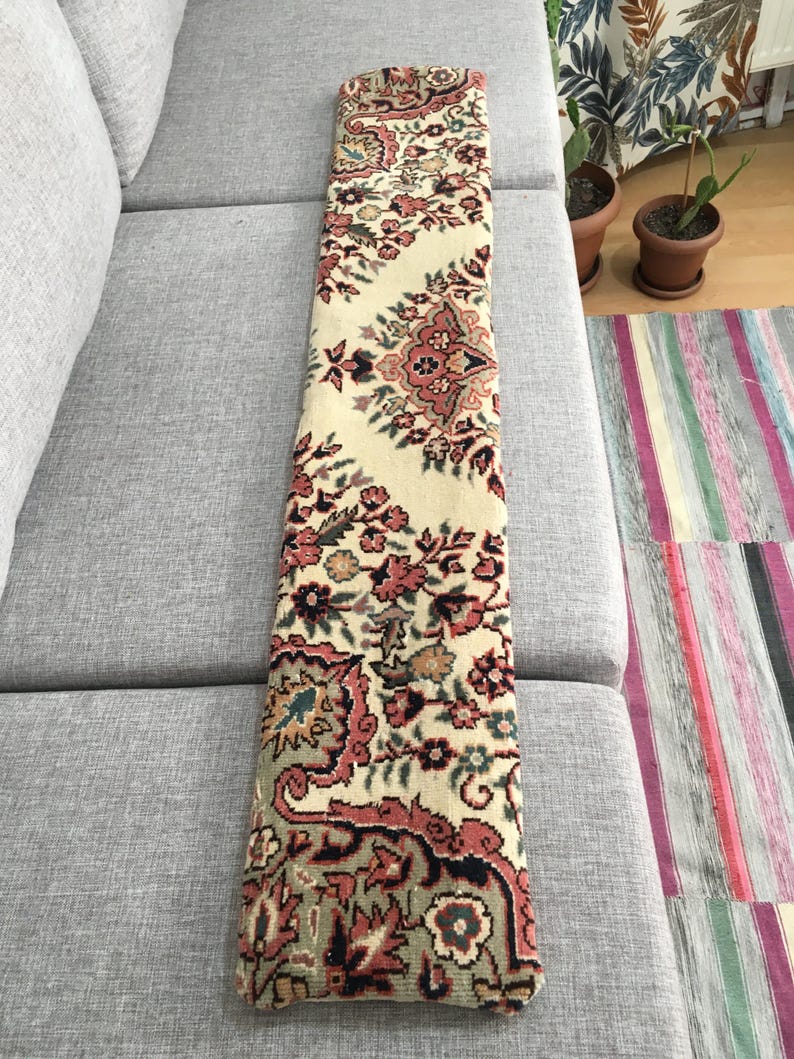 May include: A long, rectangular runner rug featuring a cream-colored background with an intricate floral pattern in shades of dusty rose, sage green, and dark charcoal. The textile displays a repeating symmetrical design with ornate botanical motifs.