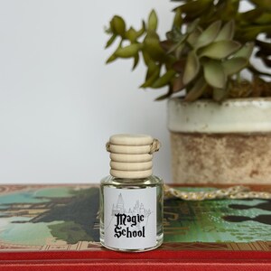 Pu&ograve; includere: Piccola bottiglia di vetro trasparente con tappo in legno ed etichetta "Magic School". La bottiglia &egrave; su un libro rosso con scritte dorate, con una pianta in vaso sullo sfondo.
