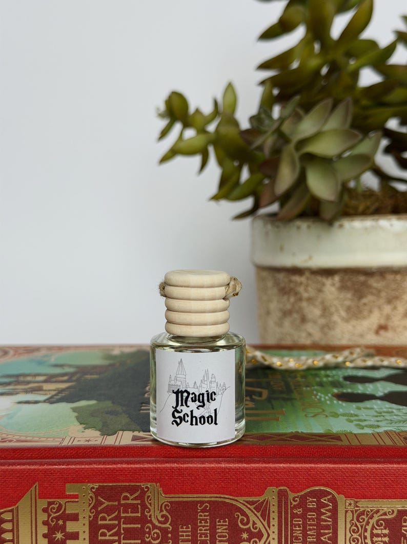 Pu&ograve; includere: Piccola bottiglia di vetro trasparente con tappo in legno ed etichetta "Magic School". La bottiglia &egrave; su un libro rosso con scritte dorate, con una pianta in vaso sullo sfondo.