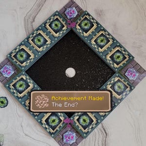 Könnte beinhalten: Rauteförmige Wanddekoration mit schwarzem Mittelteil und pixeligem Design in Türkis, Beige und Grün. Der Text "Achievement Made! The End?" wird auf einer braunen Plakette angezeigt. Dekorative Akzente sind lila und rosa Elemente.