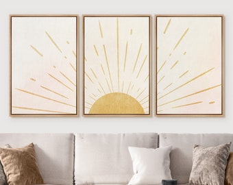 May include: Three framed prints of a stylized sun with gold rays on a white background. The middle print features a gold sun with a pink gradient in the background.