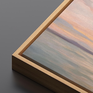 May include: A corner view of a canvas art print with a natural wood frame. The artwork features a soft, abstract landscape in shades of blue, peach, and lavender. The frame is a light brown color, and the canvas has a textured appearance.