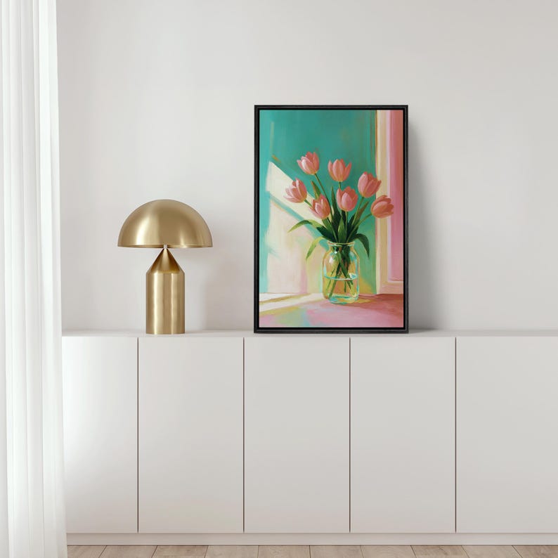 Pu&ograve; includere: Un dipinto incorniciato di tulipani rosa in un vaso di vetro trasparente, su uno sfondo turchese e rosa. L'opera d'arte &egrave; esposta su un mobile bianco, accanto a una lampada da tavolo color oro con un paralume arrotondato.