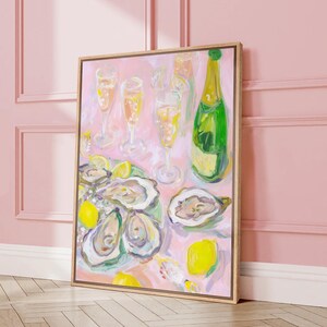 May include: A framed painting depicts a celebratory scene with champagne, oysters, and lemons. The artwork features a green champagne bottle, several filled champagne glasses, and a platter of oysters. The color palette is soft, with pinks, yellows, and greens.