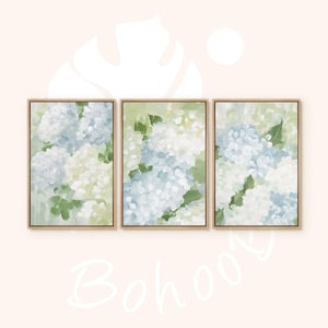 Puede incluir: Conjunto de tres l&aacute;minas art&iacute;sticas florales enmarcadas. Cada l&aacute;mina presenta una pintura de acuarela de flores de hortensia en tonos blancos, azules y verdes. La obra de arte se muestra en un marco de madera clara, creando un conjunto de arte mural coordinado.